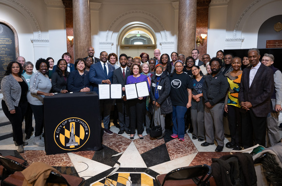 Mayor Brandon M. Scott, alongside Council President Nick Mosby and Councilman Odette Ramos, and surrounded by dozens of housing advocates and community partners holding papers